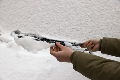 Photo of Woman cleaning car wiper blade covered with snow, closeup