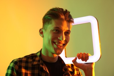 Young man with square lamp on color background in neon lights