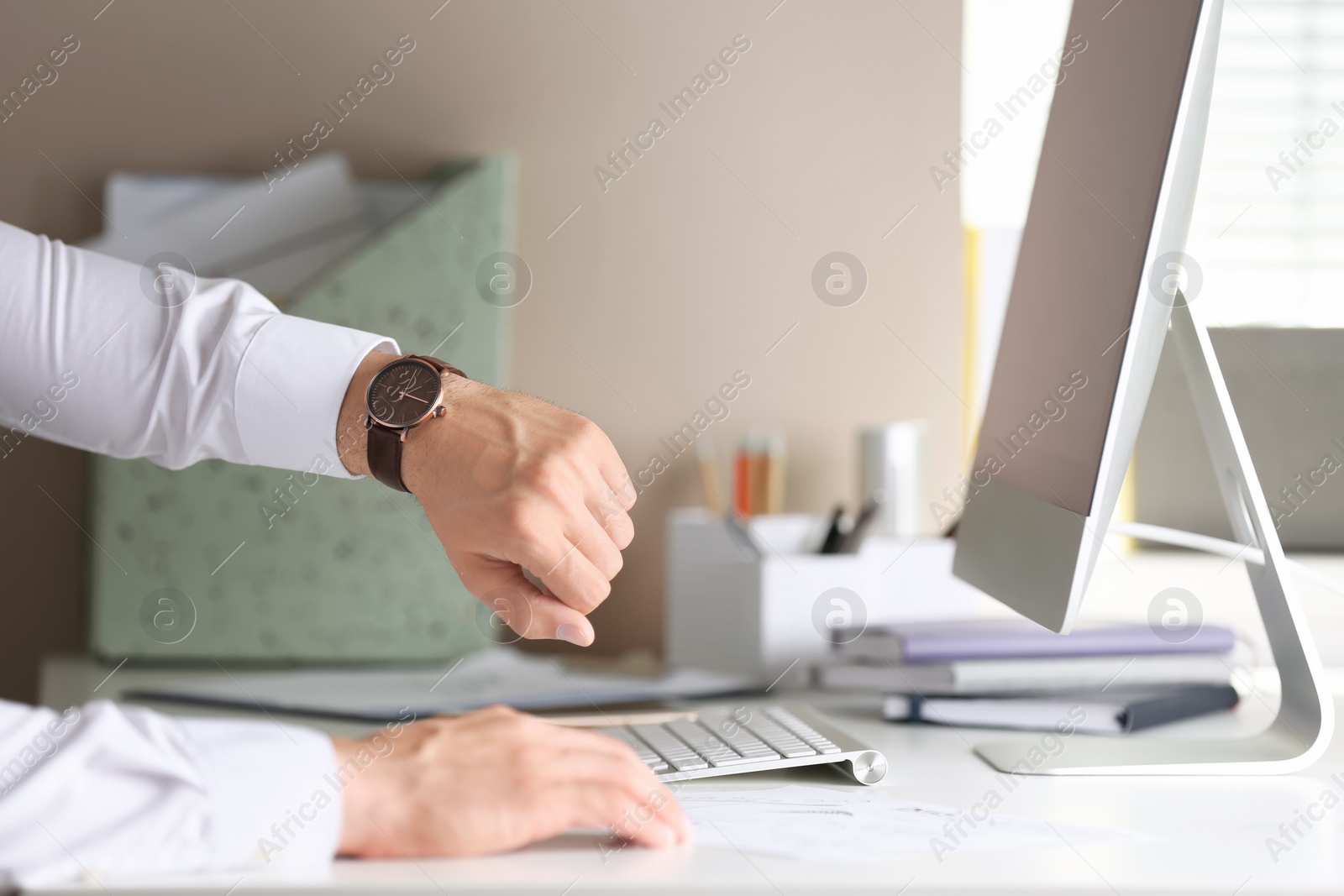 Photo of Young man checking time on his wristwatch at workplace