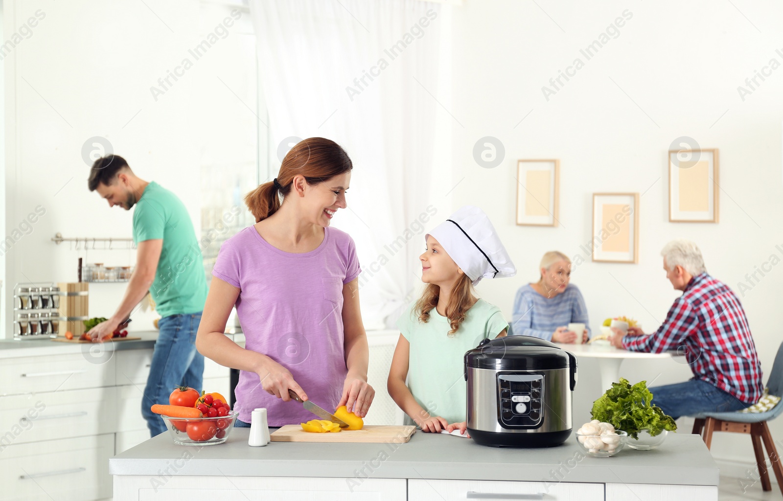 Photo of Mother and daughter preparing food with modern multi cooker in kitchen