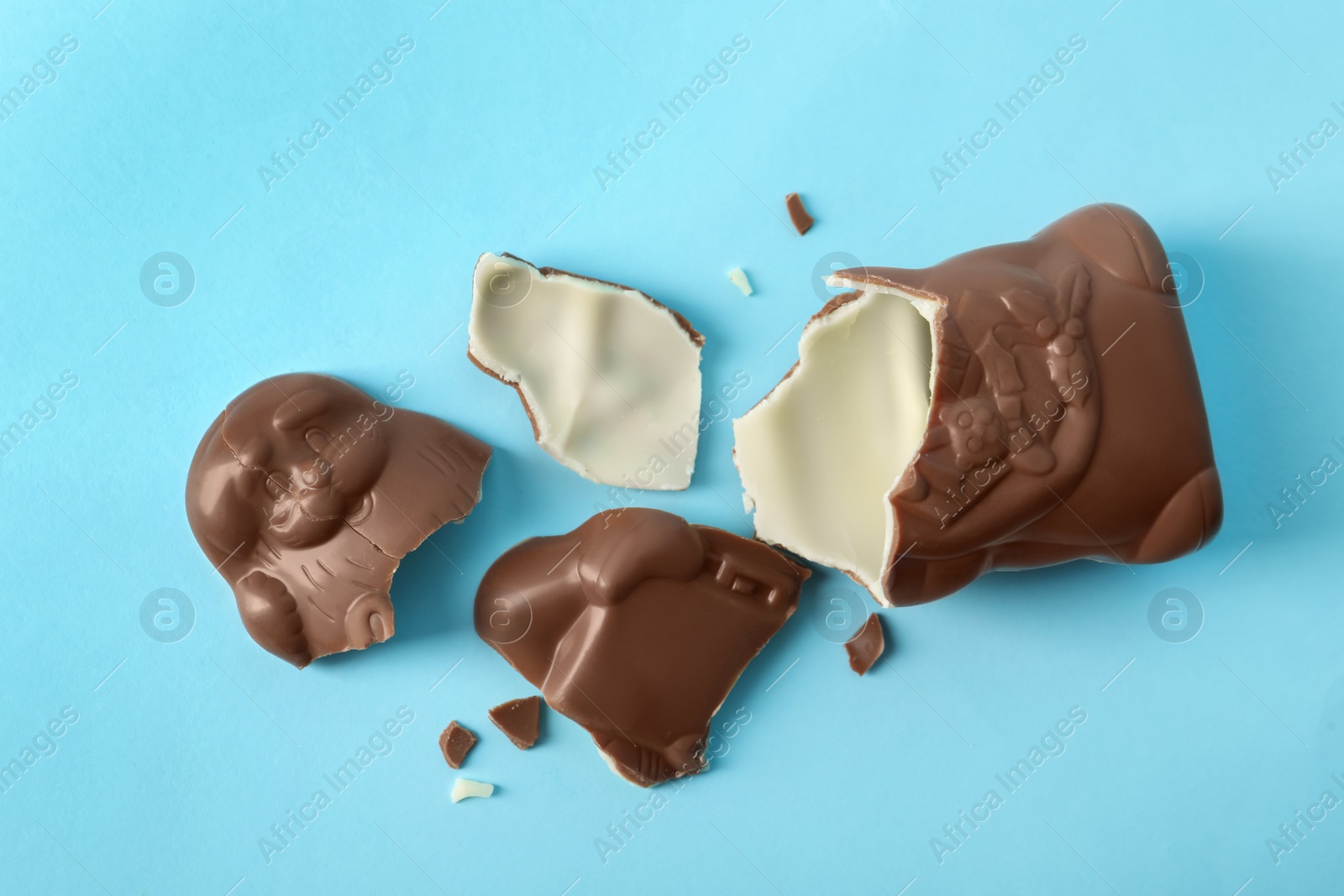 Photo of Broken chocolate Santa Claus on light blue background, flat lay