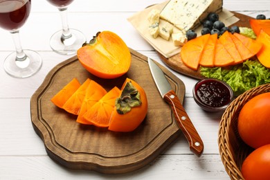 Delicious persimmon, blue cheese, blueberries and jam served on white wooden table, above view