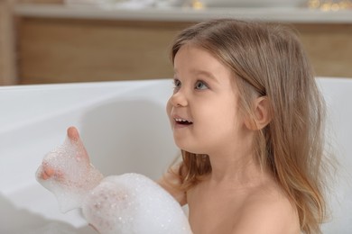 Cute little girl taking foamy bath at home. Hair washing