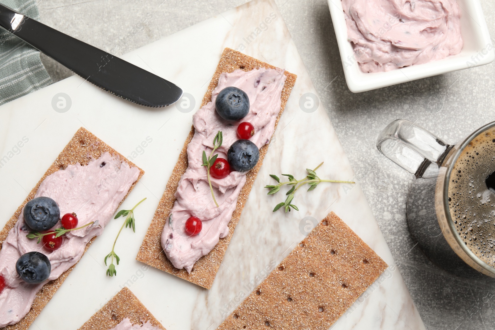 Photo of Tasty cracker sandwiches with cream cheese, blueberries, red currants, thyme and cup of coffee on grey table, flat lay