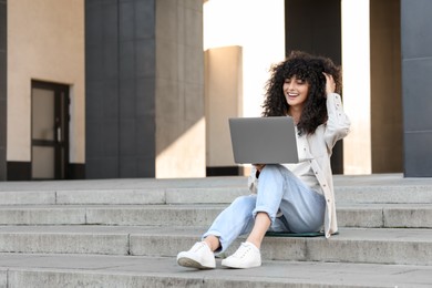 Photo of Happy young woman using modern laptop on stairs outdoors. Space for text