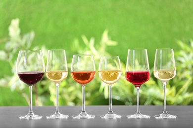 Photo of Row of glasses with different wines on grey table against blurred background