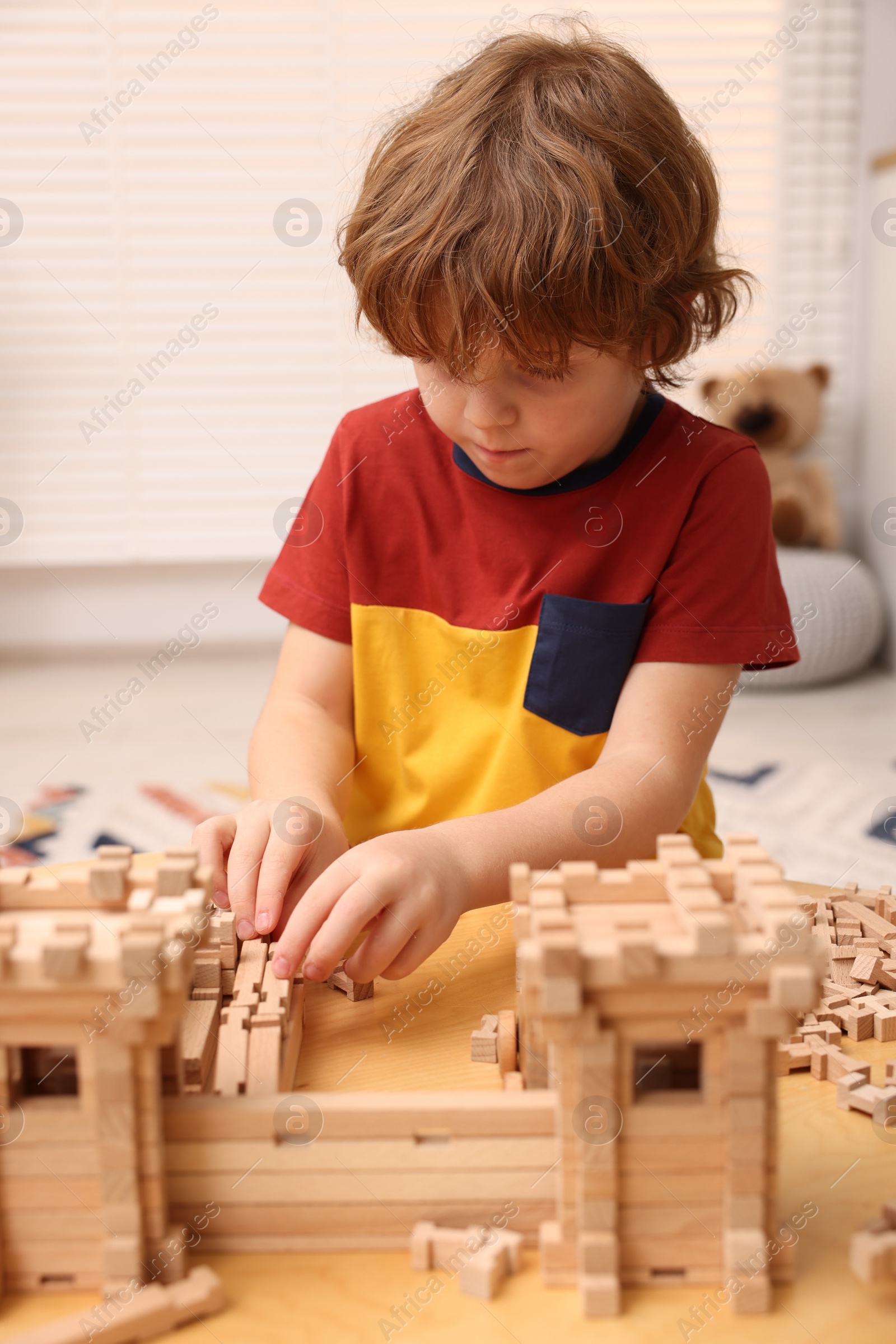 Photo of Little boy playing with wooden entry gate at table in room. Child's toy