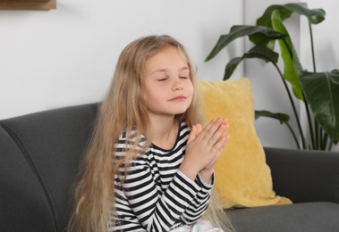 Photo of Girl with clasped hands praying on sofa at home