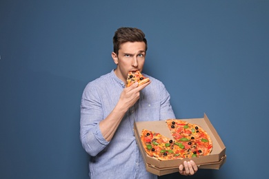 Attractive young man with delicious pizza on color background