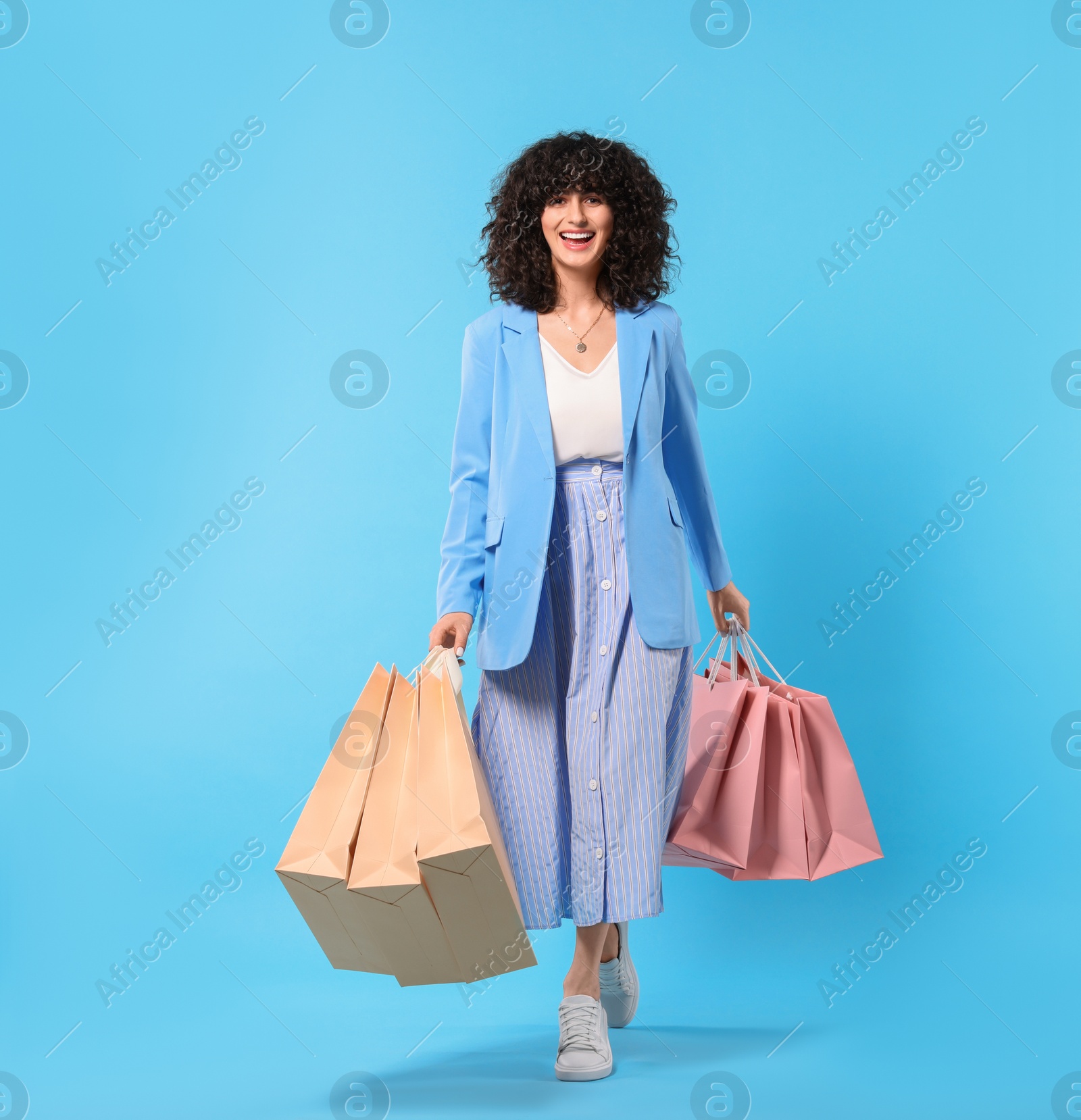 Photo of Happy young woman with shopping bags on light blue background