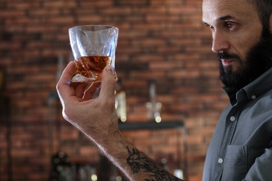 Photo of Handsome man holding glass of whiskey indoors