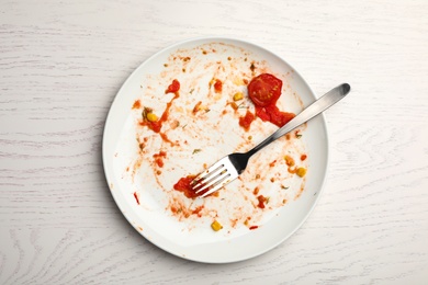 Photo of Dirty plate with food leftovers and fork on white wooden background, top view