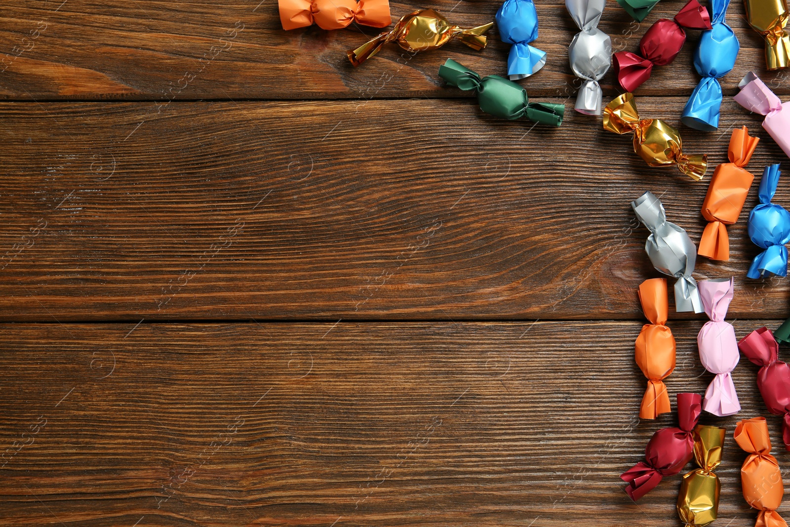 Photo of Many candies in colorful wrappers on wooden table, flat lay. Space for text