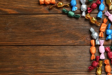 Photo of Many candies in colorful wrappers on wooden table, flat lay. Space for text