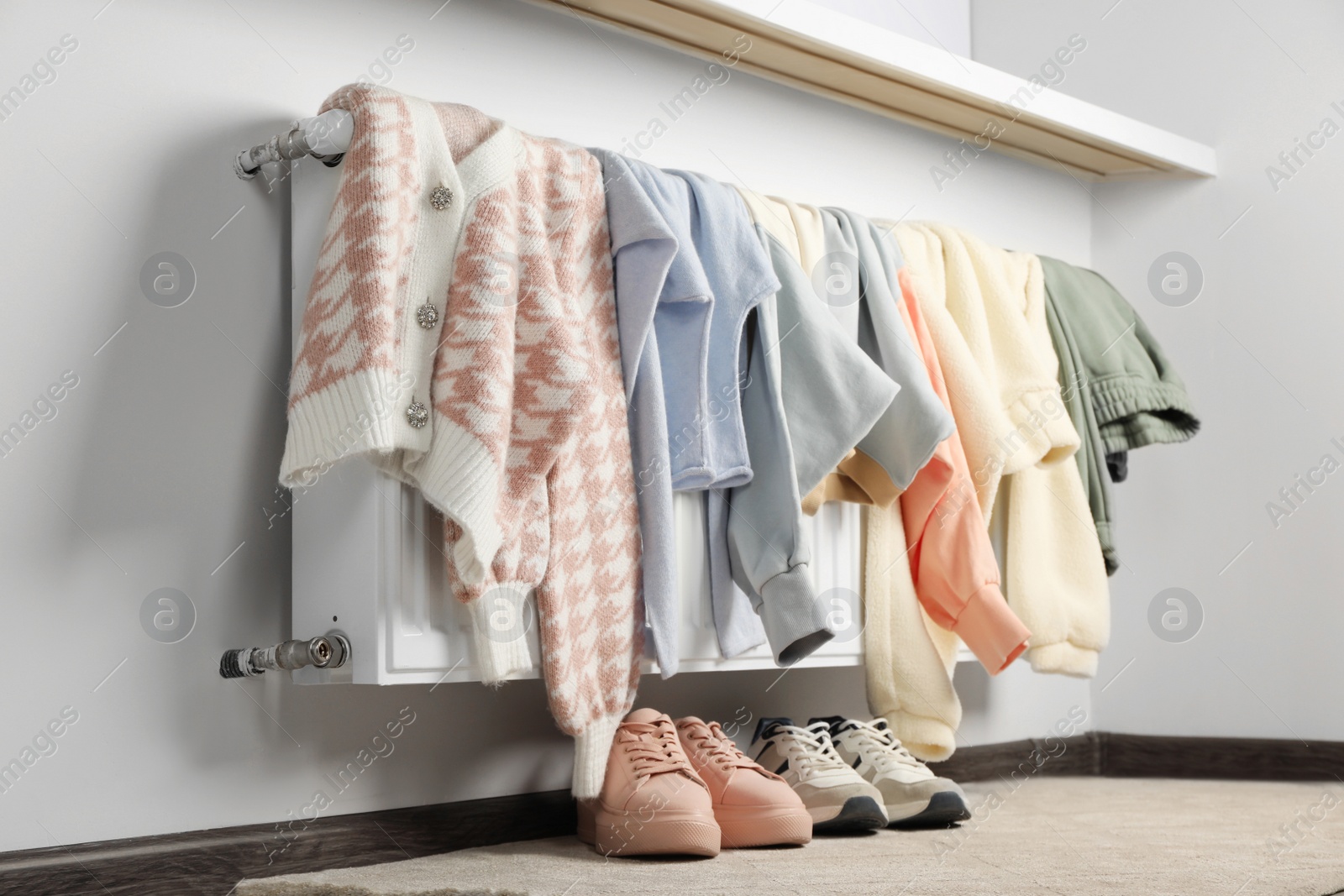 Photo of Heating radiator with clothes and shoes in room