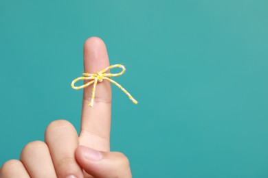 Photo of Man showing index finger with tied bow as reminder on turquoise background, closeup. Space for text