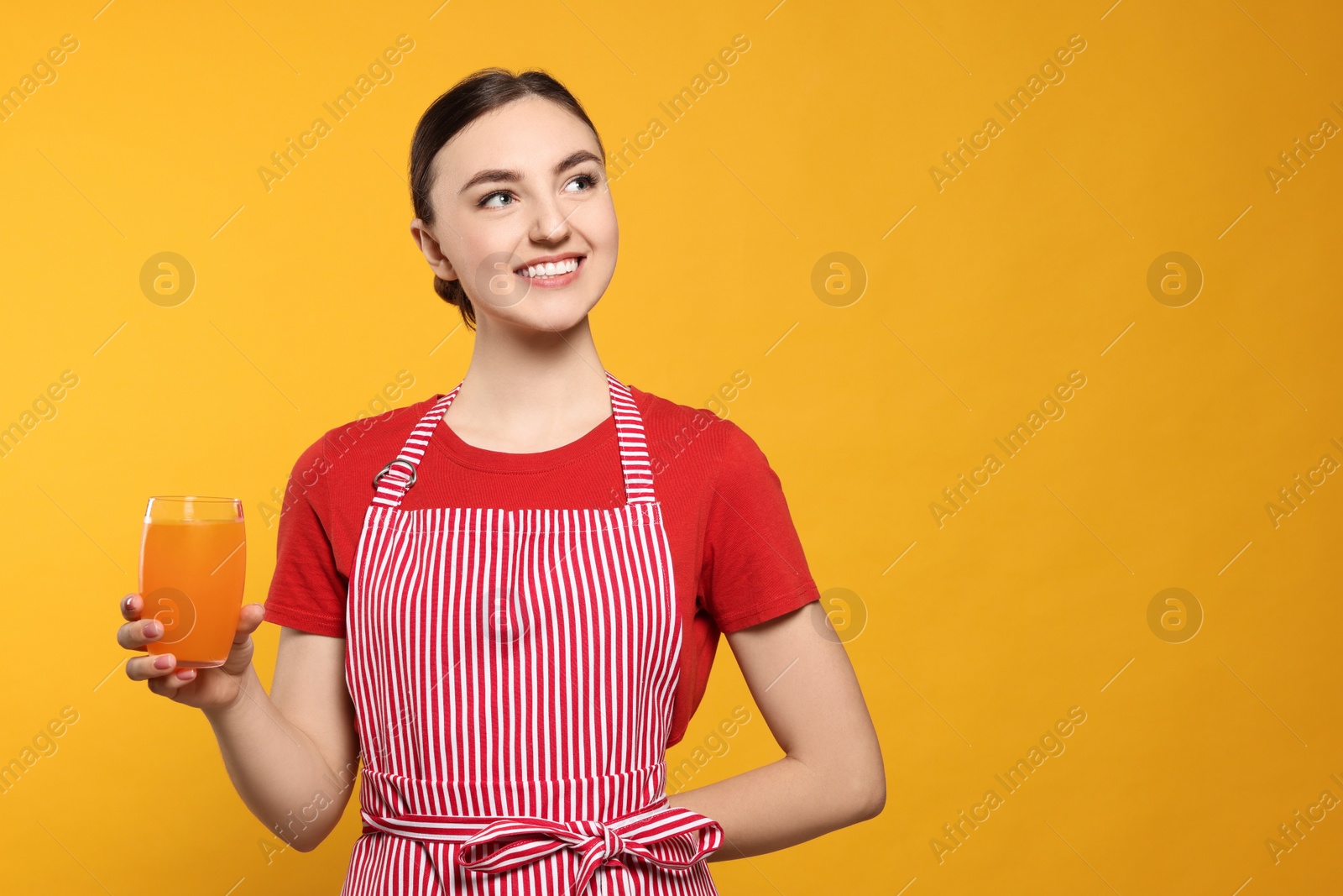 Photo of Beautiful young woman in clean striped apron with glass of juice on orange background. Space for text