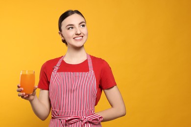 Photo of Beautiful young woman in clean striped apron with glass of juice on orange background. Space for text