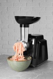 Photo of Electric meat grinder with chicken mince on grey marble table near white wall