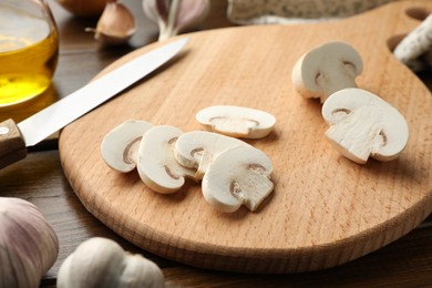 Photo of Cutting board with mushrooms and knife on wooden table, closeup