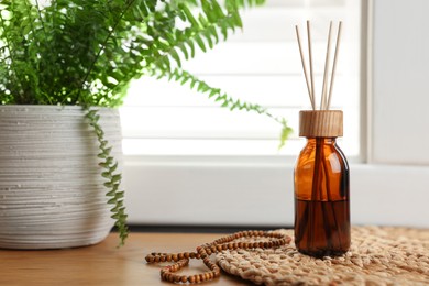 Photo of Air reed freshener, beads and houseplant on wooden table indoors