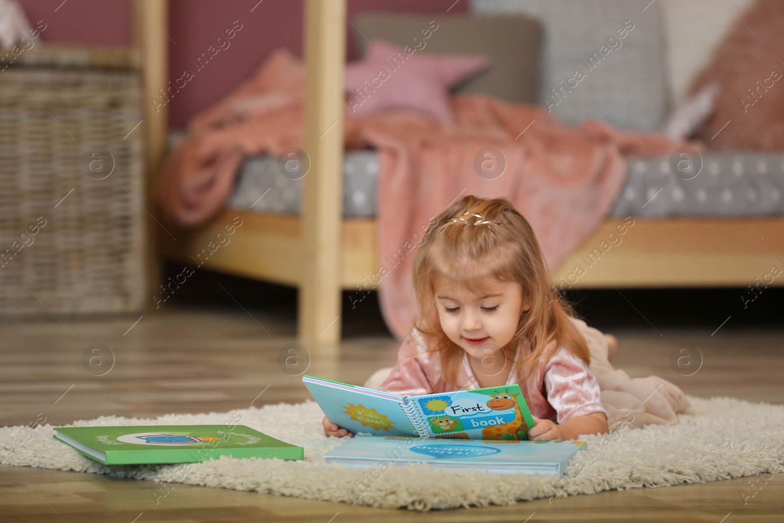 Photo of Cute little girl in princess dress reading book at home