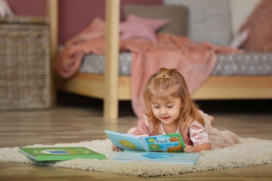 Photo of Cute little girl in princess dress reading book at home