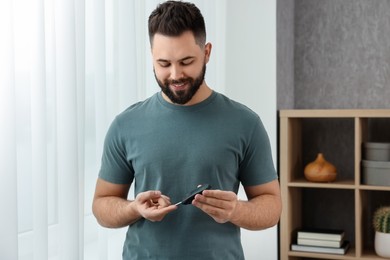 Photo of Diabetes test. Smiling man checking blood sugar level with lancet pen at home