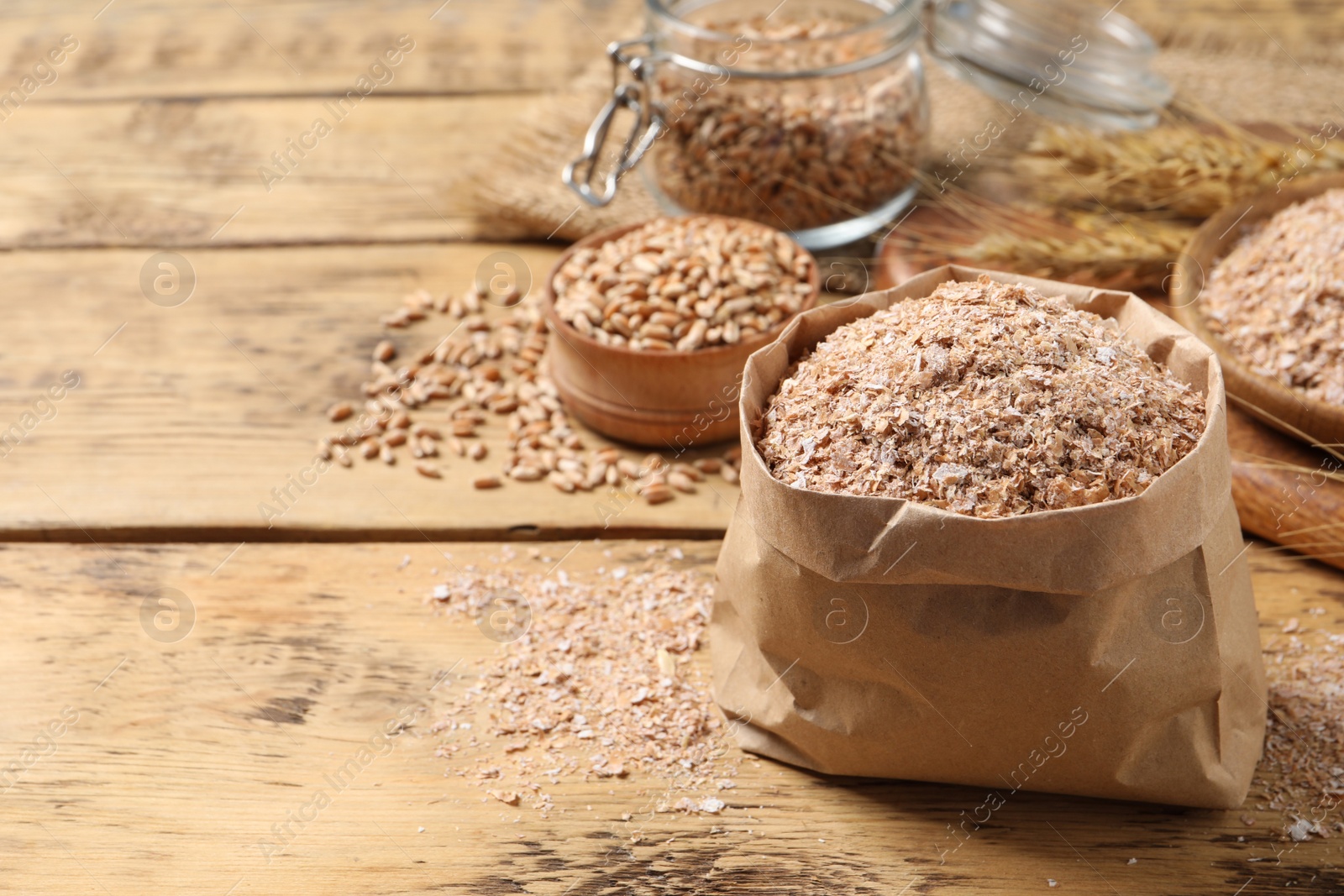 Photo of Paper bag with wheat bran on wooden table, space for text