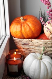 Wicker basket with pumpkins, beautiful heather flowers and burning candles near window indoors