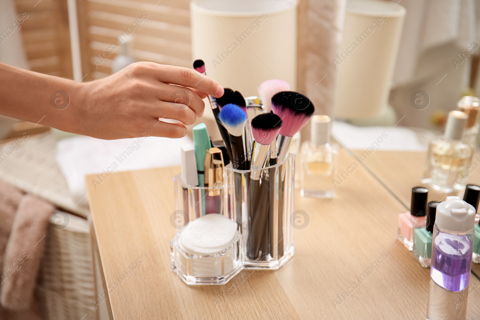 Photo of Woman taking brush from organizer for makeup cosmetic products on table