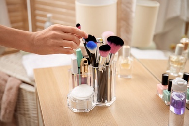 Woman taking brush from organizer for makeup cosmetic products on table