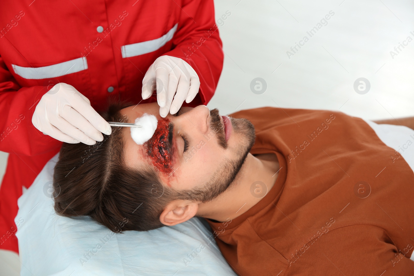 Photo of Nurse cleaning young man's head injury in clinic. First aid