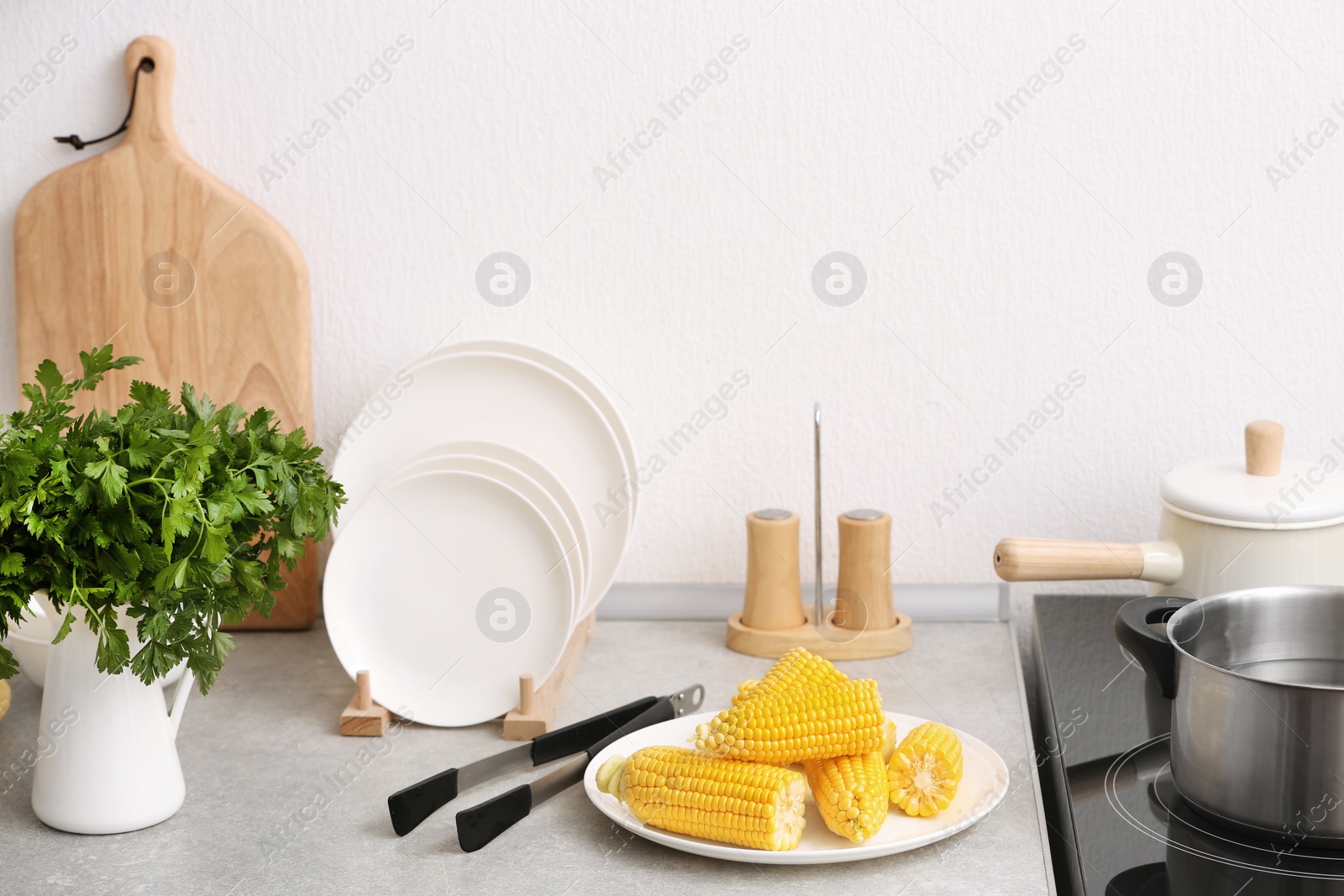 Photo of Plate with ripe corn cobs and tongs on kitchen table. Space for text