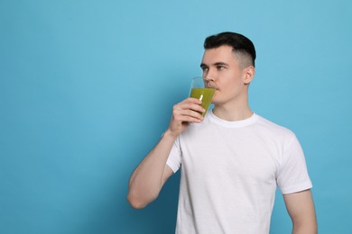 Photo of Handsome young man drinking juice on light blue background, space for text