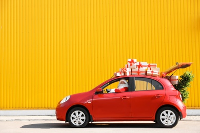 Authentic Santa Claus driving red car with gift boxes and Christmas tree, view from outside