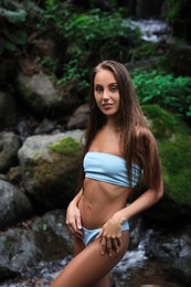 Photo of Beautiful young woman in light blue bikini near mountain stream outdoors