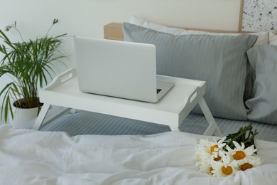 Photo of White tray table with laptop and bouquet of beautiful daisies on bed indoors
