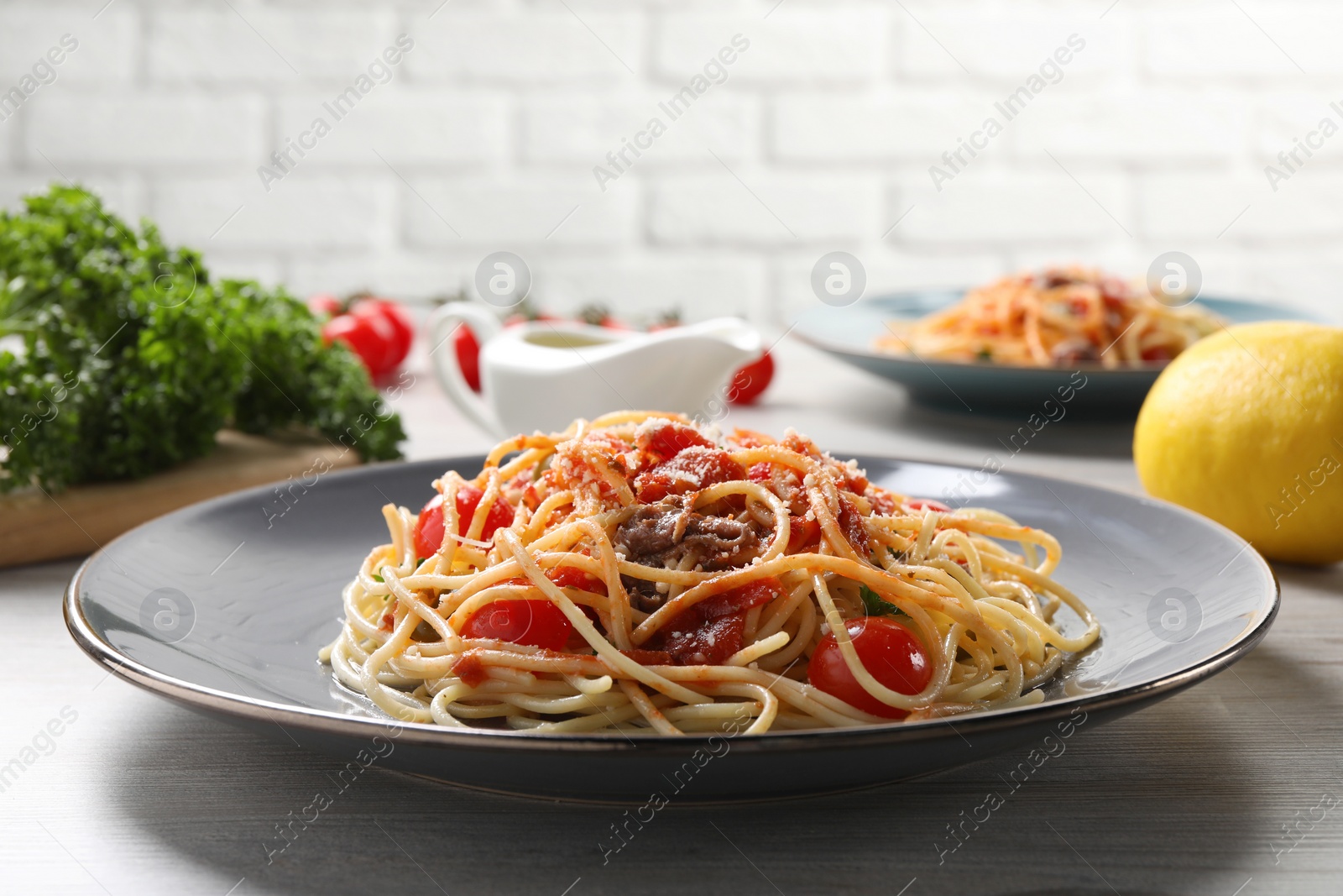 Photo of Delicious pasta with anchovies, tomatoes and parmesan cheese served on white wooden table