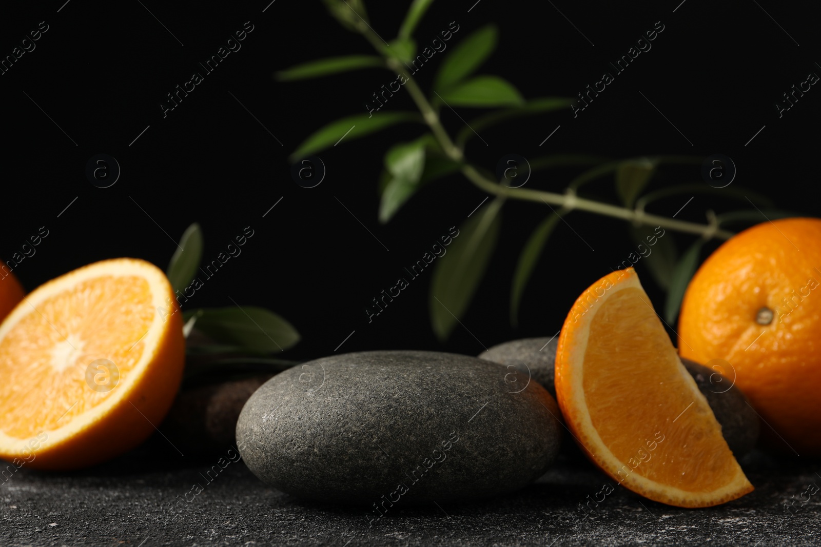 Photo of Tasty fresh oranges, stones and leaves on black table, closeup