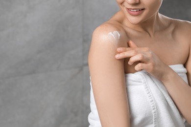Photo of Young woman applying body cream onto shoulder near grey wall, closeup. Space for text