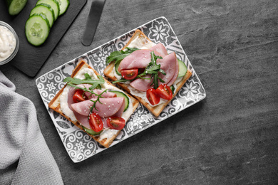 Tasty sandwiches with ham served on grey table, flat lay