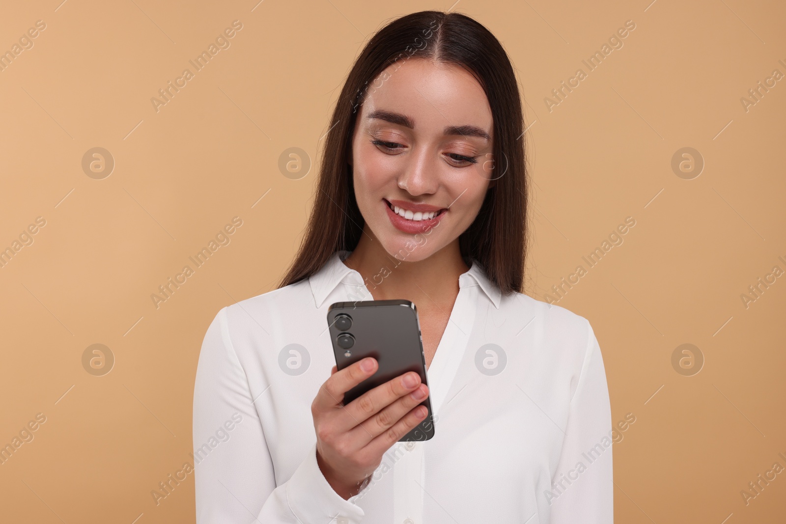Photo of Happy young woman looking at smartphone on beige background