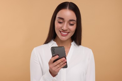 Happy young woman looking at smartphone on beige background