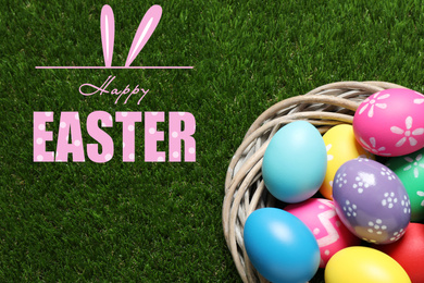 Image of Colorful eggs in decorative nest and text Happy Easter on green grass, top view