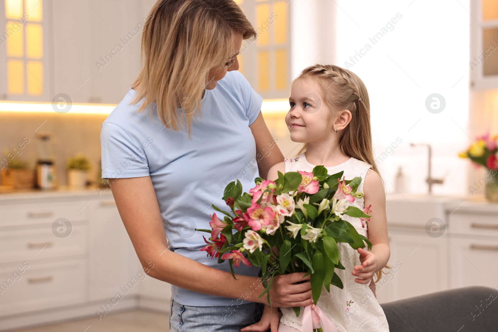 Photo of Little daughter congratulating her mom with bouquet of alstroemeria flowers in kitchen. Happy Mother's Day