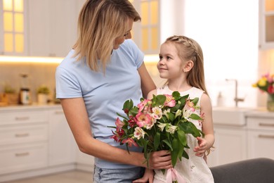 Little daughter congratulating her mom with bouquet of alstroemeria flowers in kitchen. Happy Mother's Day