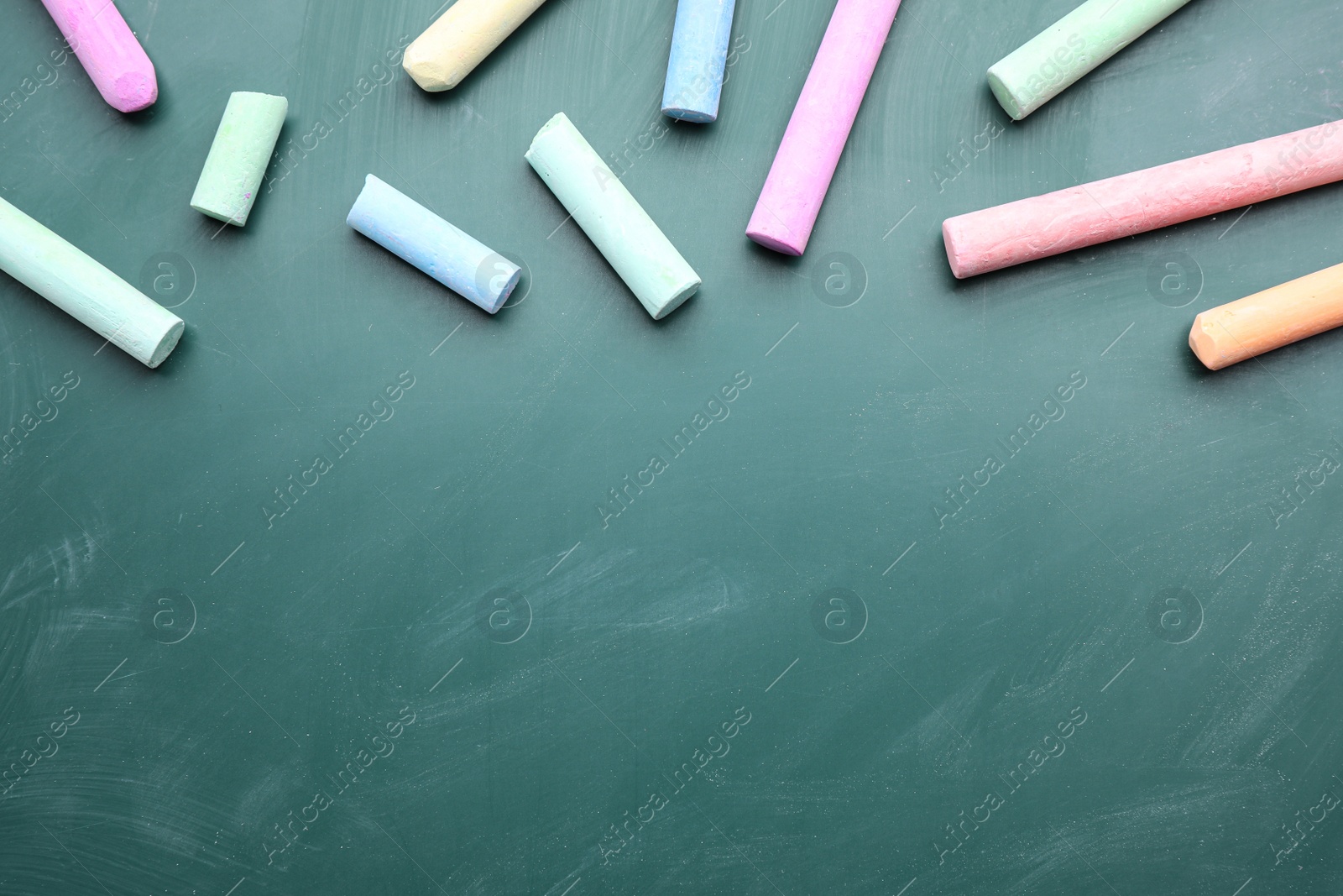 Photo of Pieces of color chalk on greenboard, flat lay. Space for text