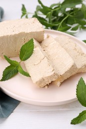 Plate with pieces of tasty halva and mint on white wooden table, closeup