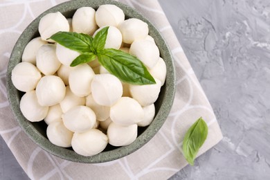 Photo of Tasty mozzarella balls and basil leaves in bowl on grey table, top view. Space for text